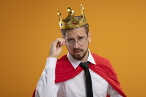 thinking young superhero guy wearing tie and crown wearing and grabbed glasses isolated on orange background چگونه شخصیت یک شاه را پرورش دهیم - گامی فراتر از عنوان